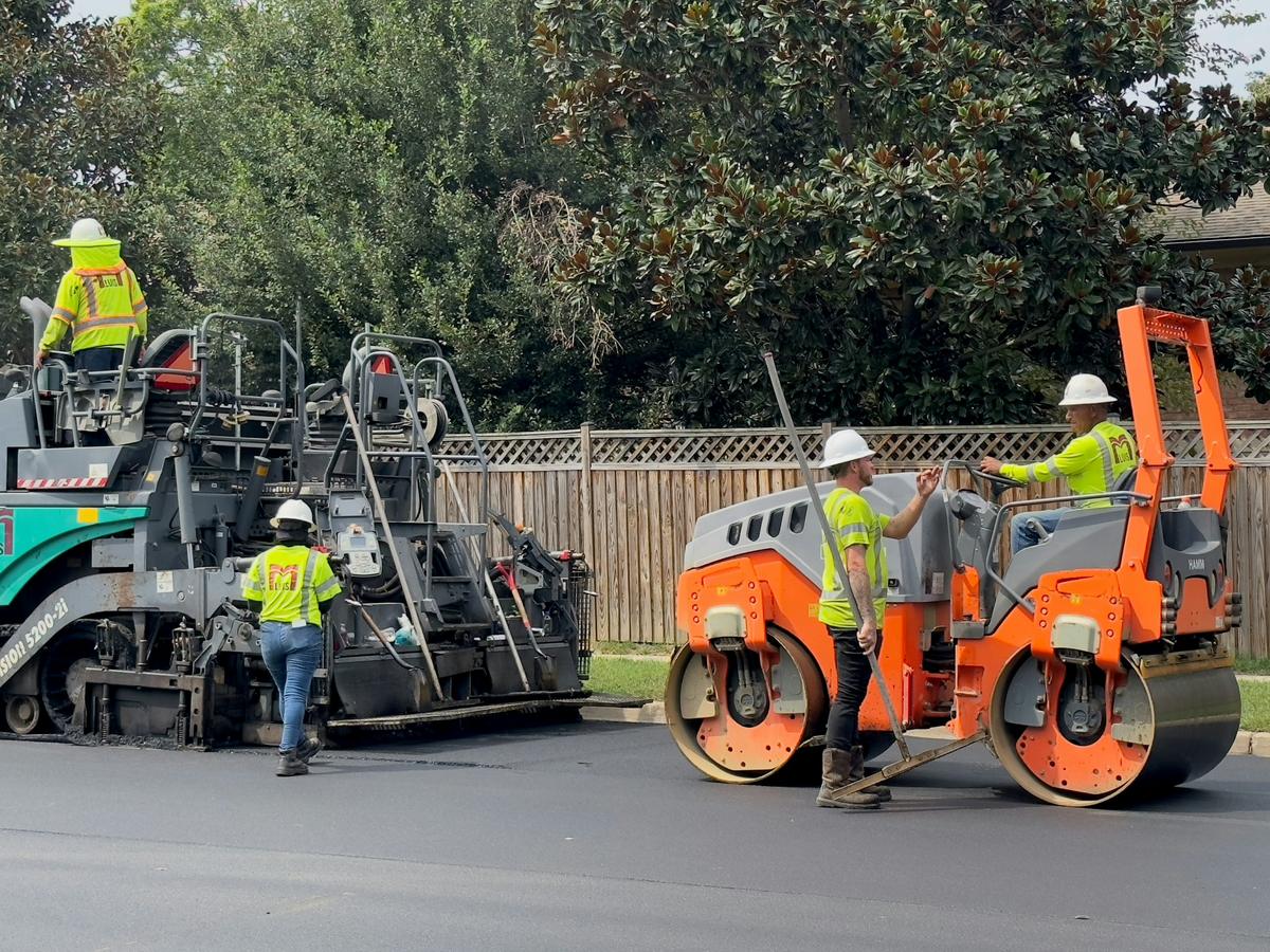 Road crew operating a paver and compaction roller during resurfacing
